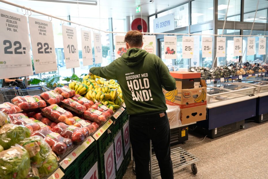 Ung medarbejder fylder varer op i frugt og grønt i en REMA 1000 butik