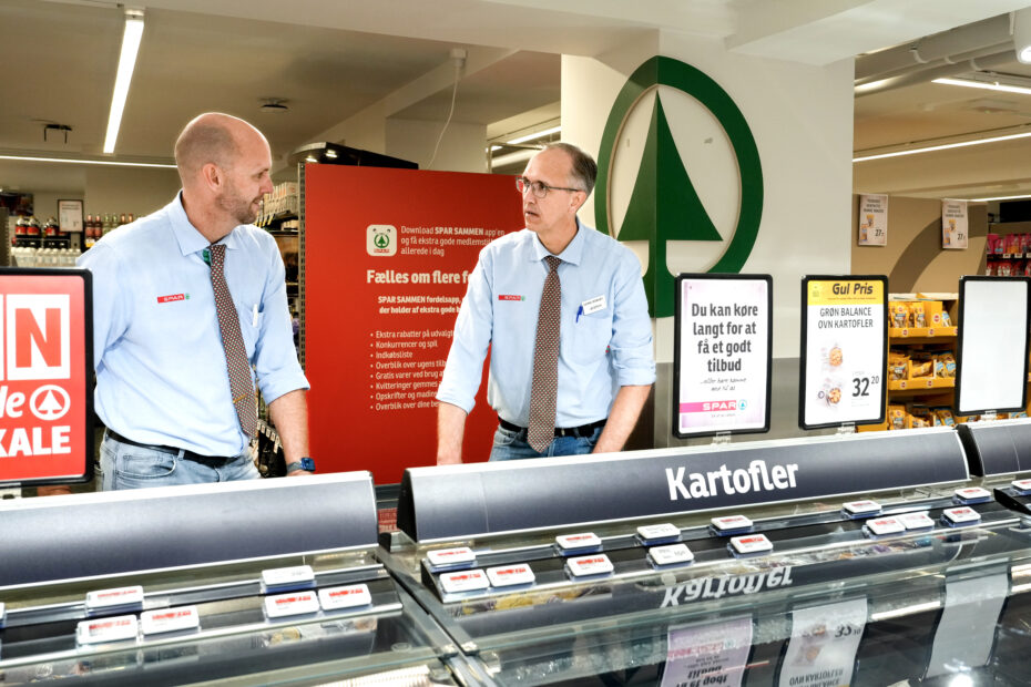To købmænd taler sammen ved køledisken i en købmandsbutik